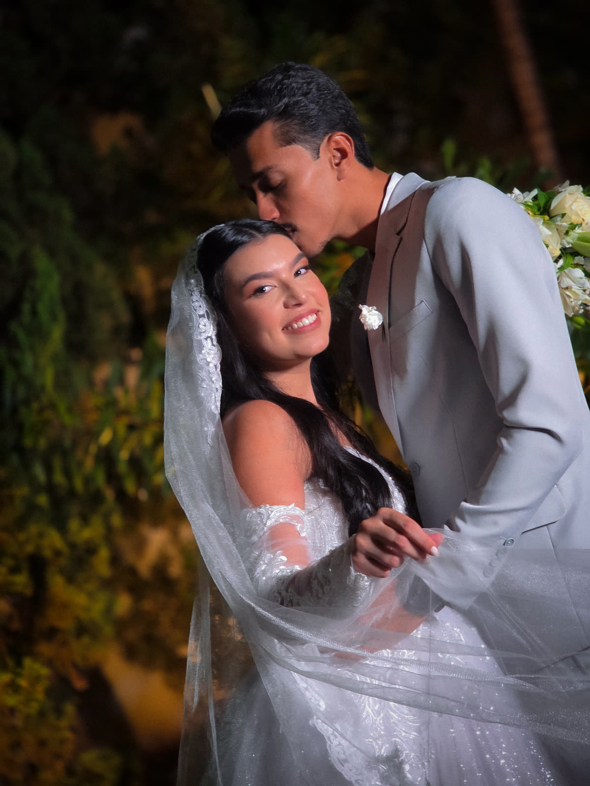 Noivo beijando a testa da noiva à noite, no jardim